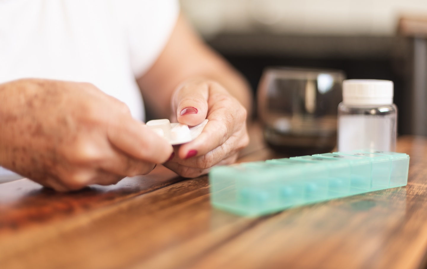 A woman holds a pill bottle in one hand and a glass of water in the other, preparing to take medication.