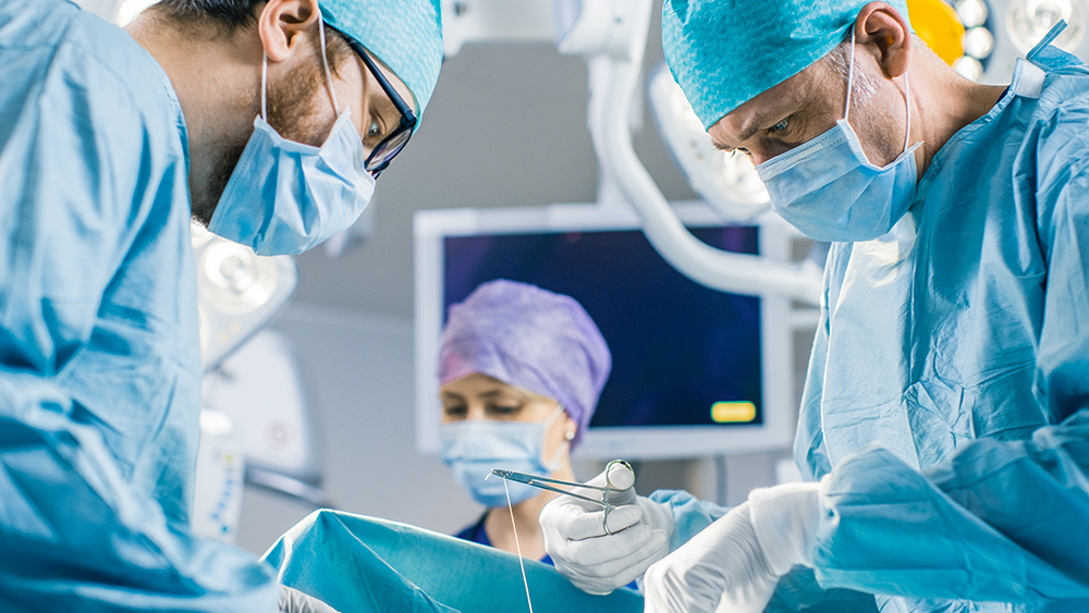 Three healthcare professionals, dressed in surgical gowns, masks, and gloves, are performing surgery