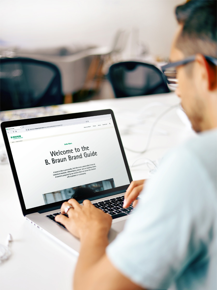 A man in a light blue shirt operating a laptop with the B. Braun website open.
