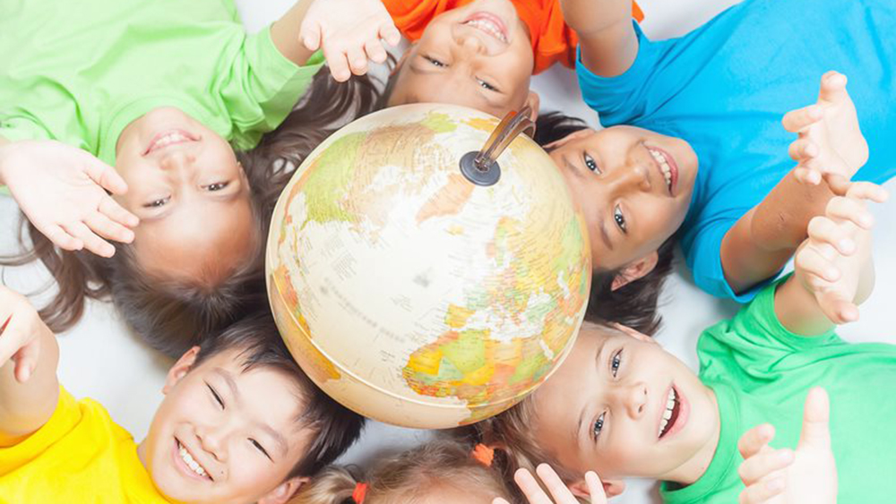 Smiling kids laying around a globe on the ground while stretching their arms upwards.